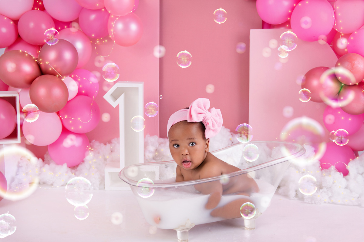 Smiling baby girl sitting in bubble bath with number one prop – Pretoria first birthday photographer.